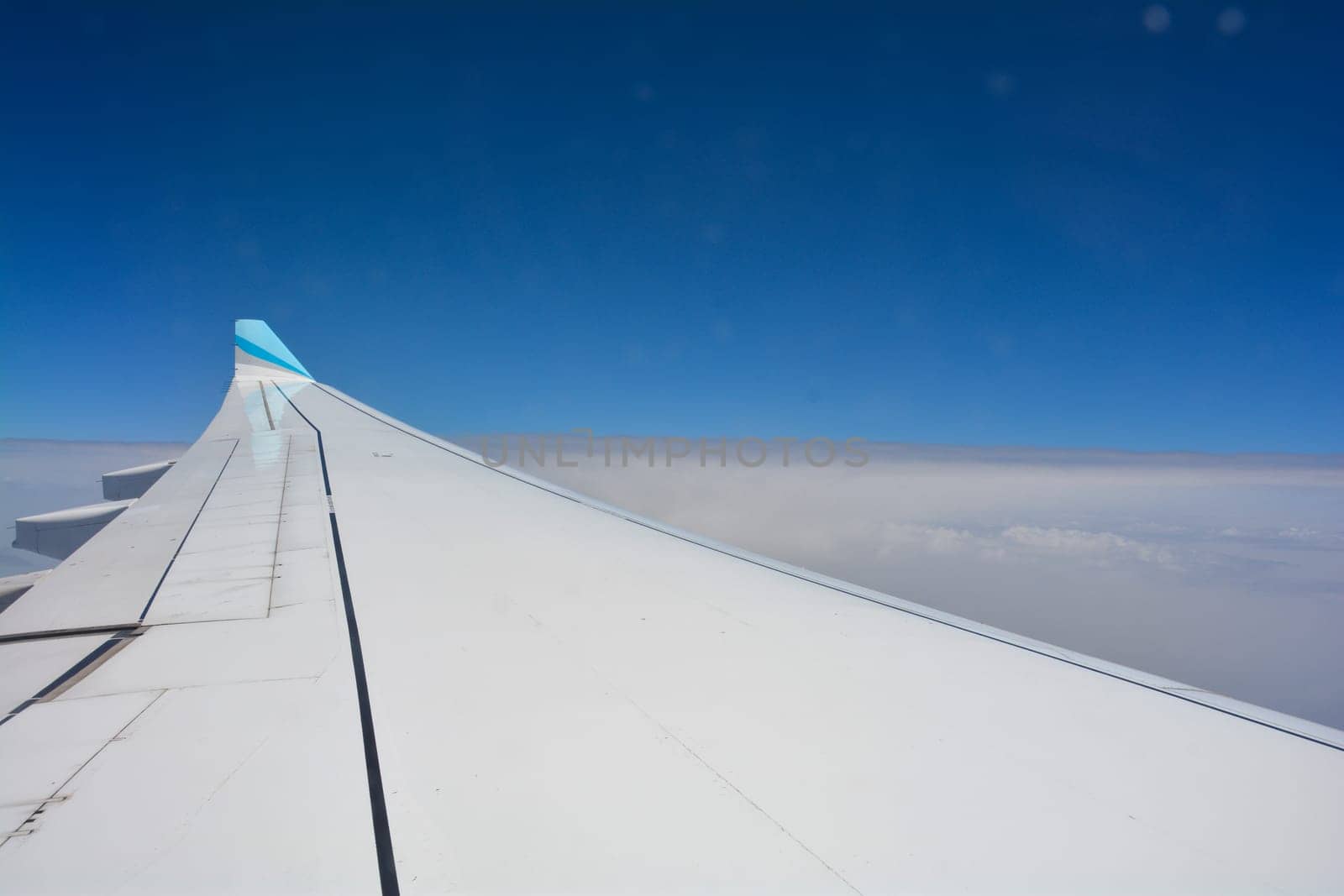 Looking out of an airplane window showing a plane wing with blue sky and white clouds