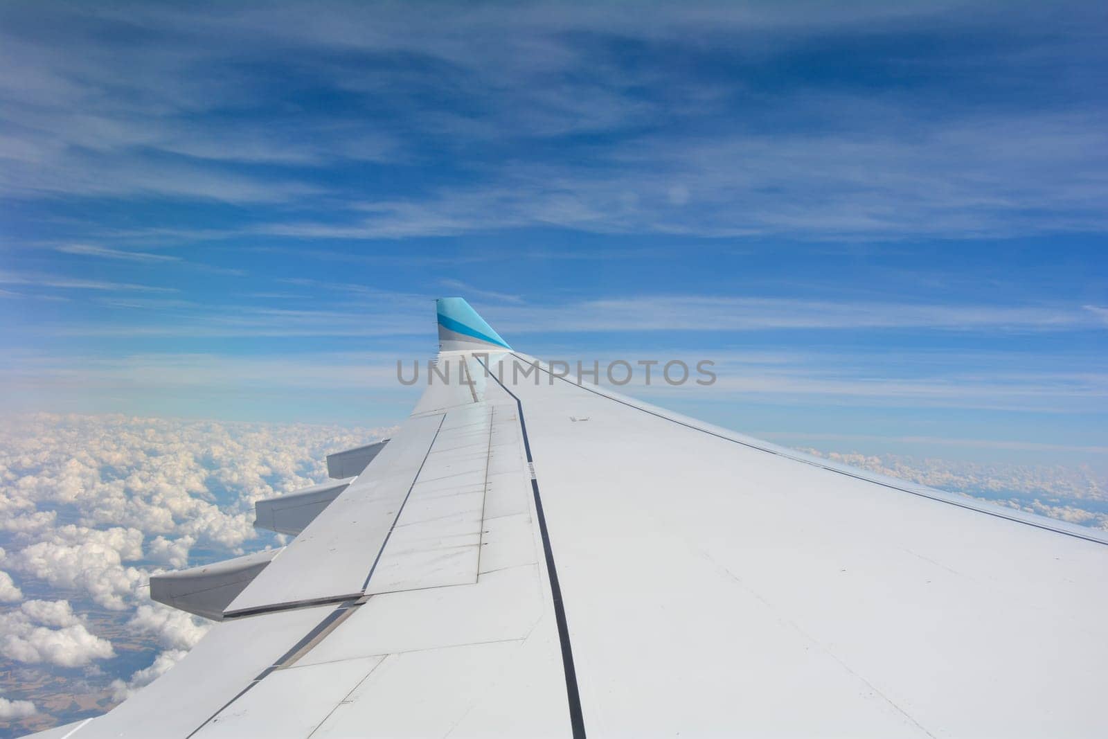 Looking out of an airplane window showing a plane wing with blue sky and white clouds