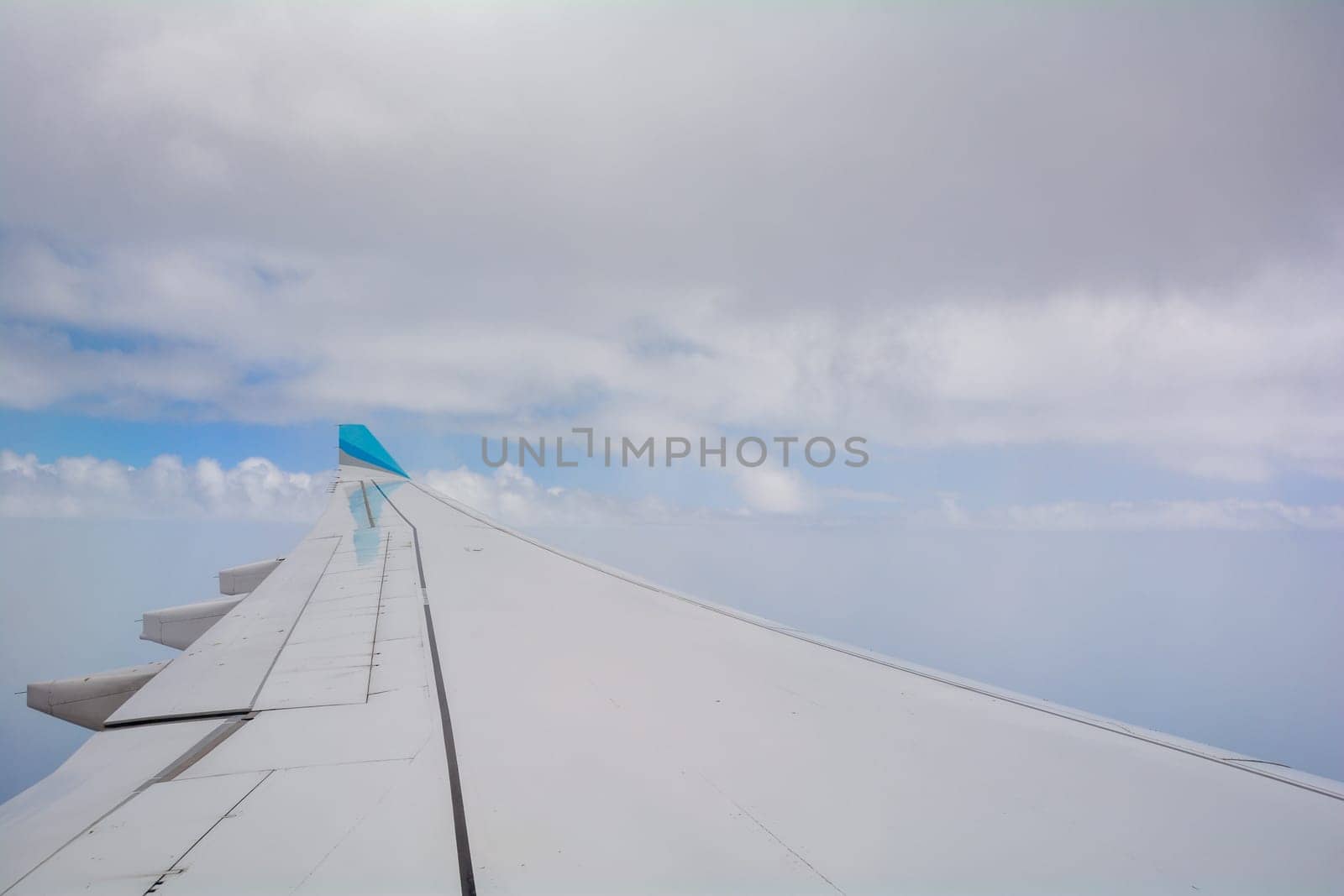 Looking out of an airplane window showing a plane wing with blue sky and white clouds