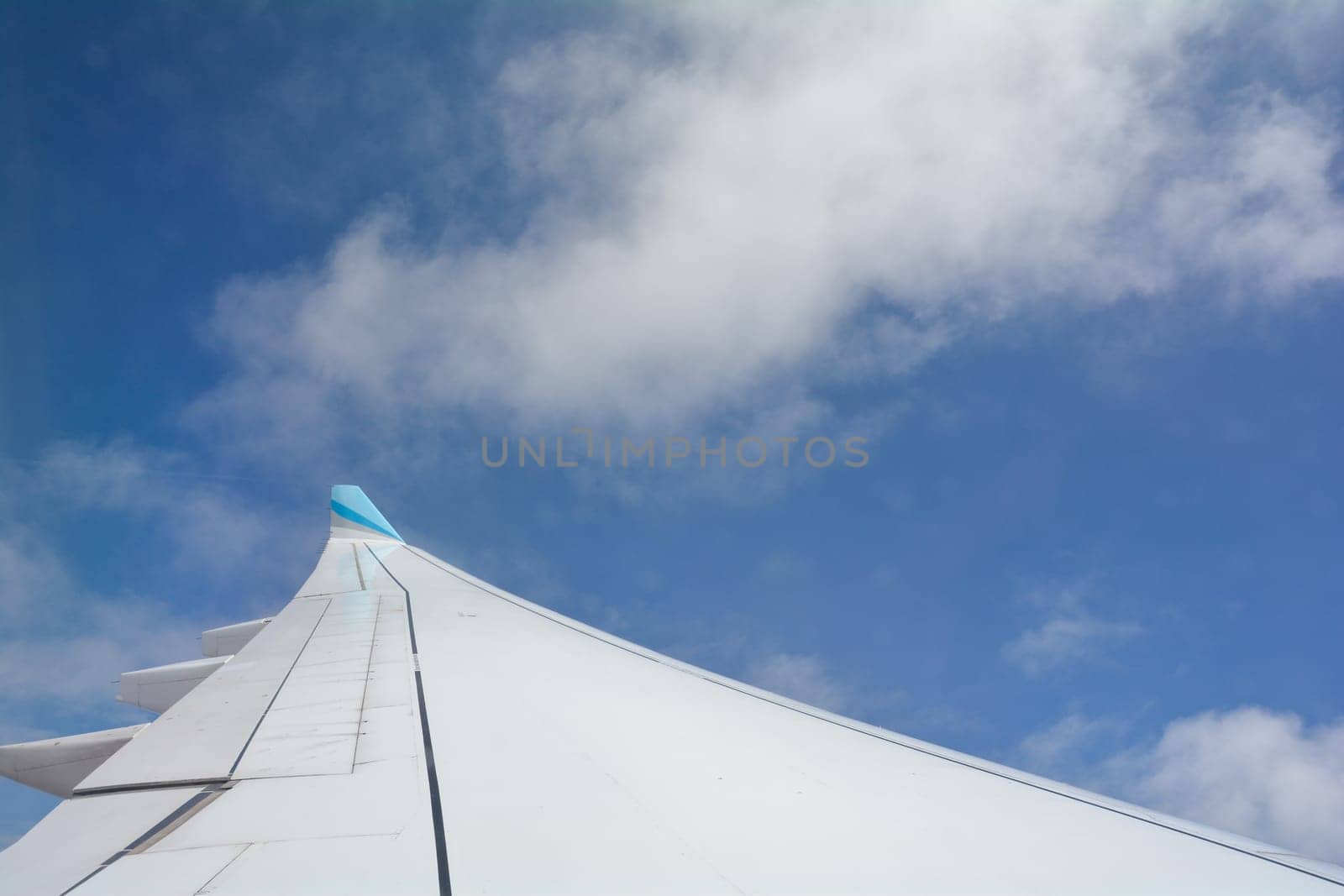 Looking out of an airplane window showing a plane wing with blue sky and white clouds