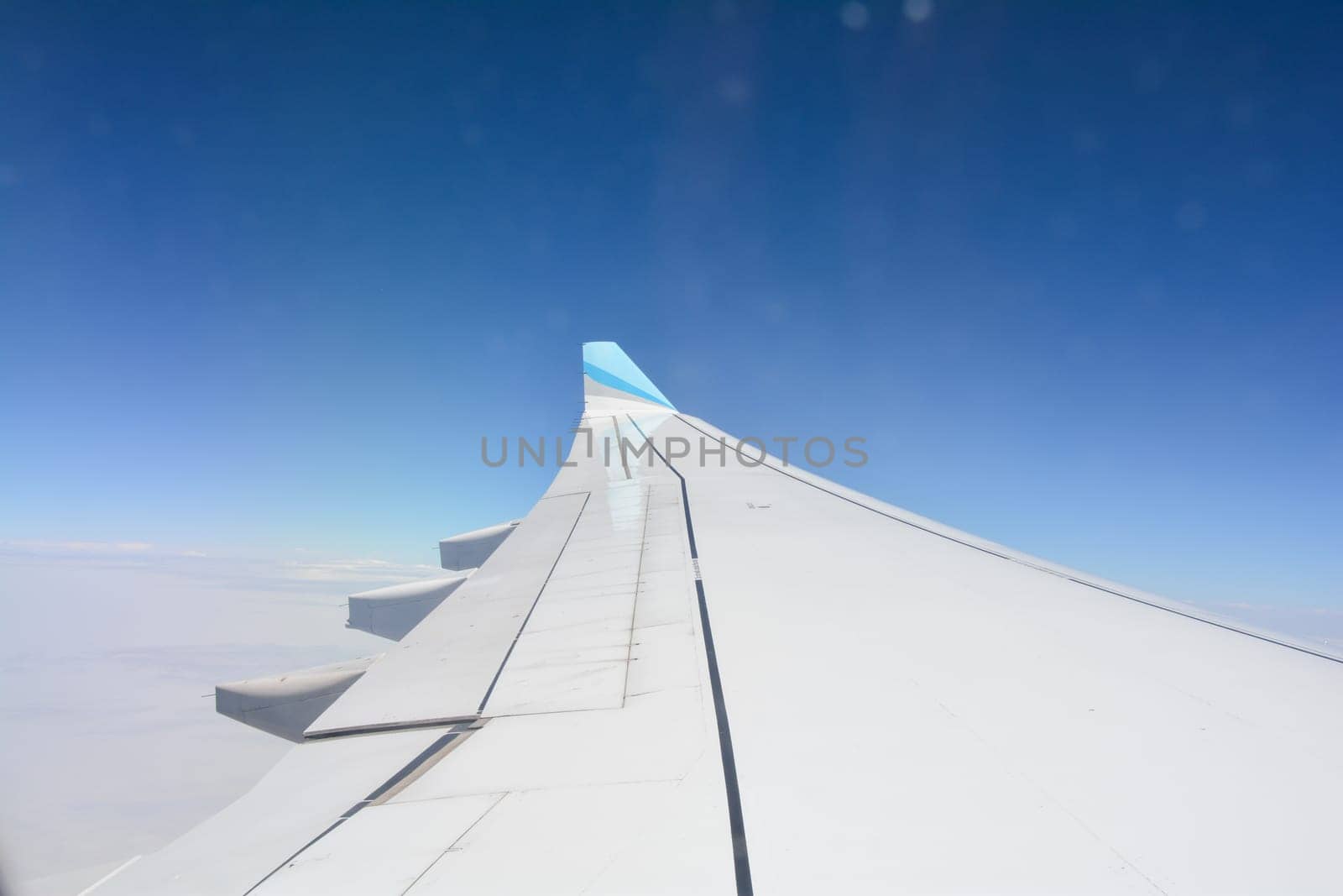 Looking out of an airplane window showing a plane wing with blue sky and white clouds