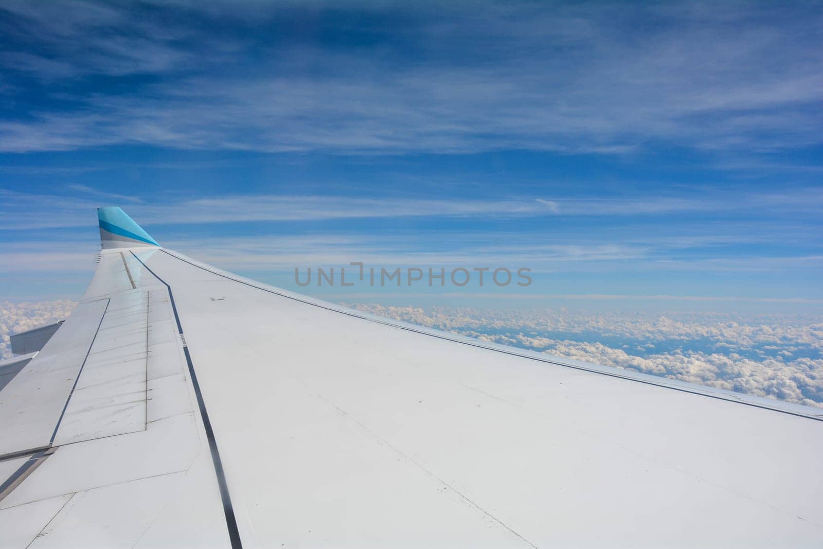 Looking out of an airplane window showing a plane wing with blue sky and white clouds