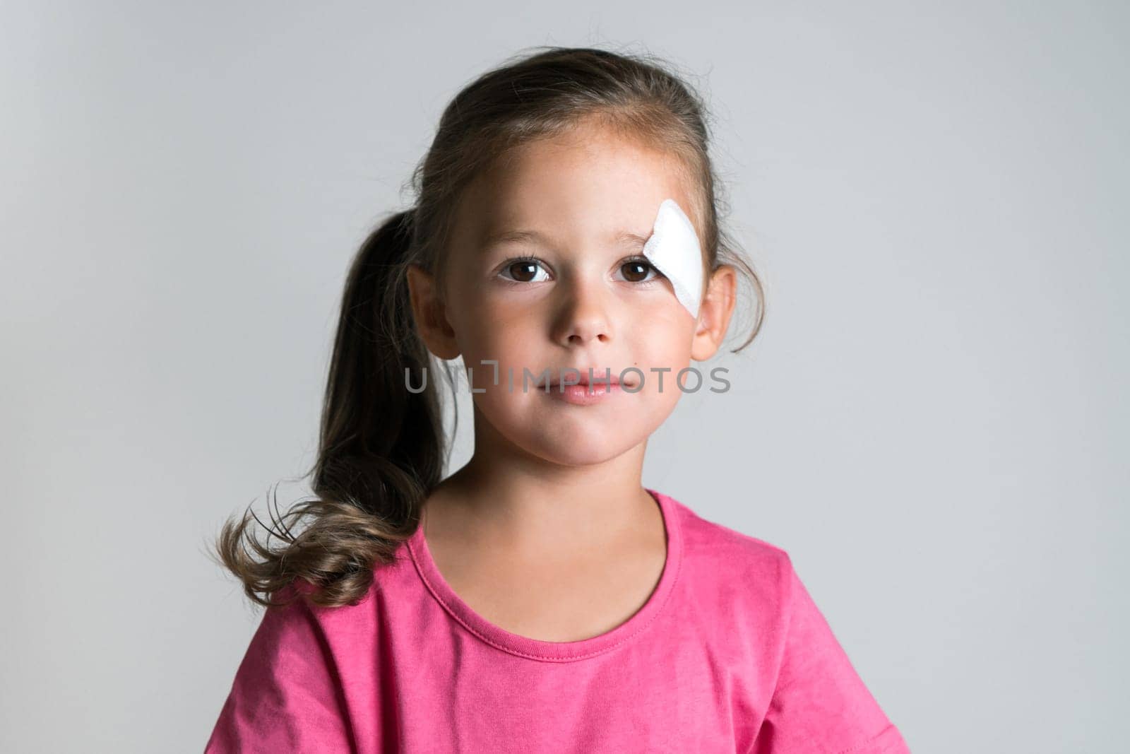 Close up nice, cute, lovely, adorable dark haired little child, girl with bandage covering injury, scratch on face. Child abuse and physical wounds. Poor children and family problems, social issues
