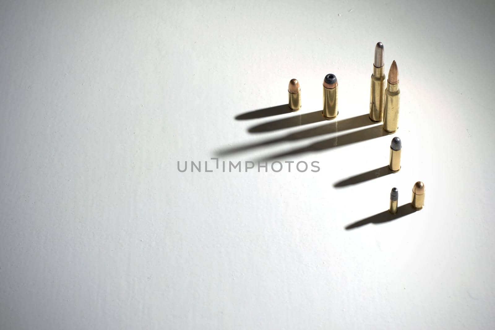 Bullets of different calibers standing on a white surface with dark, dramatic shadows.