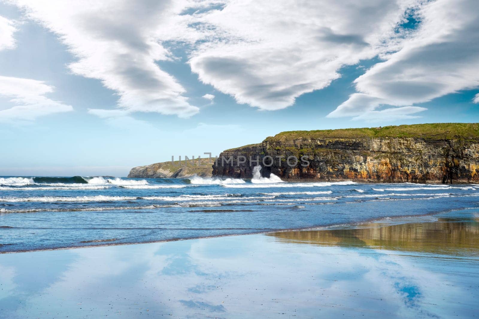 reflection of cliffs and clouds on a wet sandy ballybunion beach in ireland