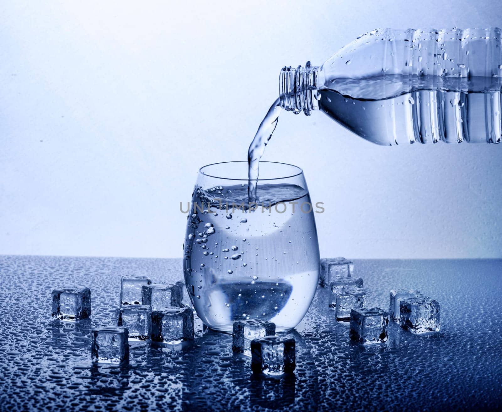 Pouring fresh drinking mineral water from plastic bottle. Glass filled with water over white background.
