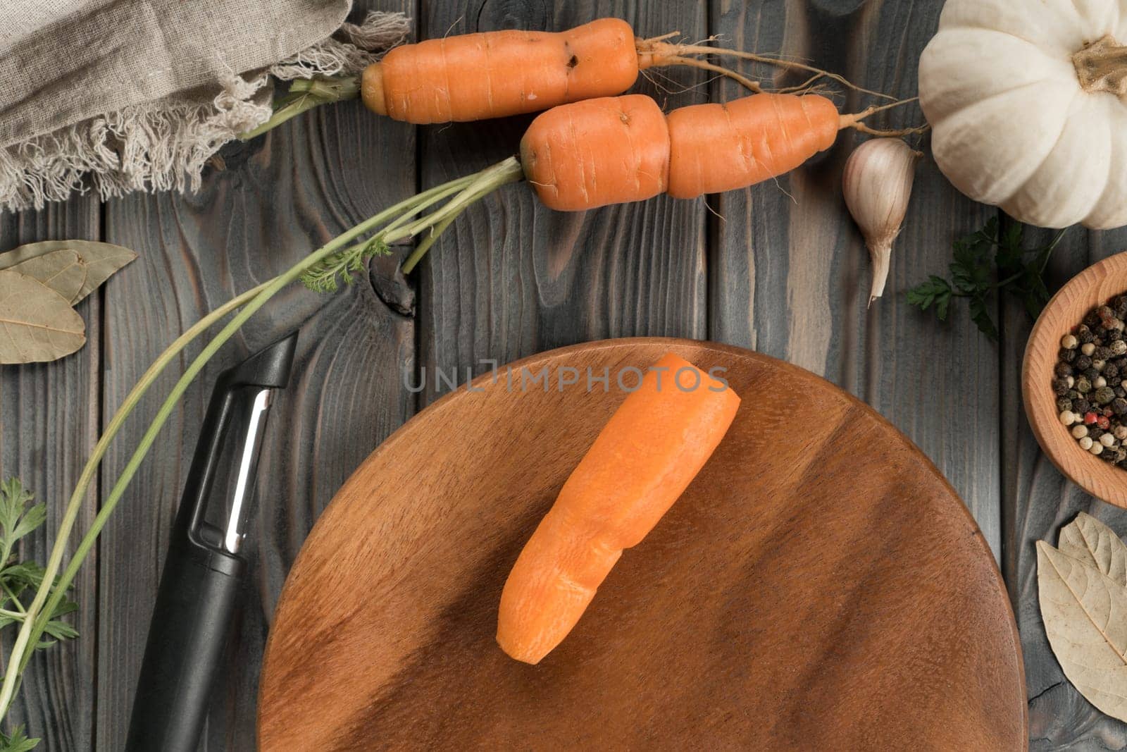 Peeling ripe orange carrot with vegetable peeler. Flat lay view. Fresh peeled carrot. Cutting peel on kitchen wooden board. Prepare ingredients for cooking, recipe. Vegetables and flavorings.