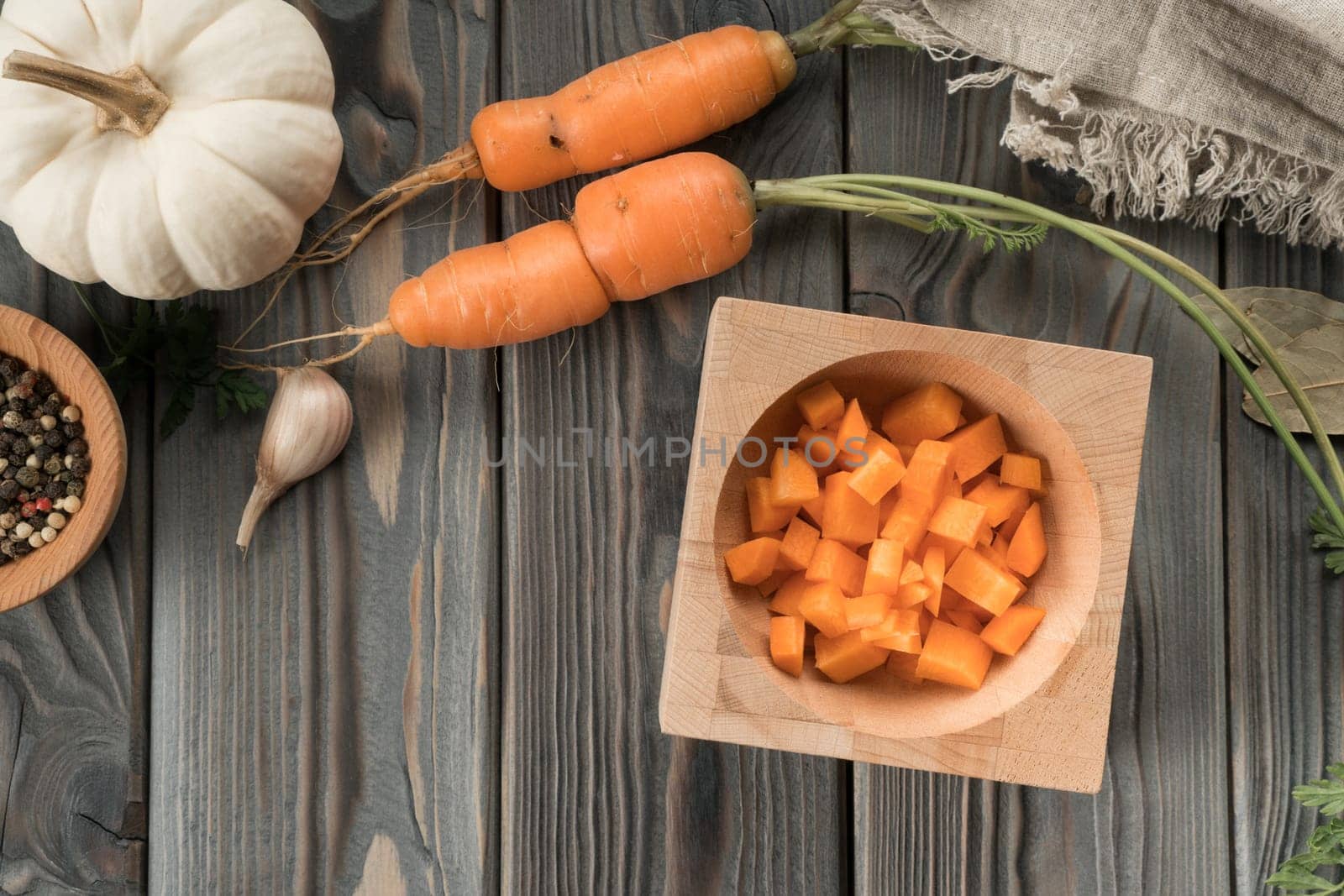 Cut ripe raw orange carrot into cubes. Diced carrot in bowl on kitchen wooden table. Flat lay view. Layout of fresh vegetables and flavorings. Prepare ingredients for cooking. Healthy food.