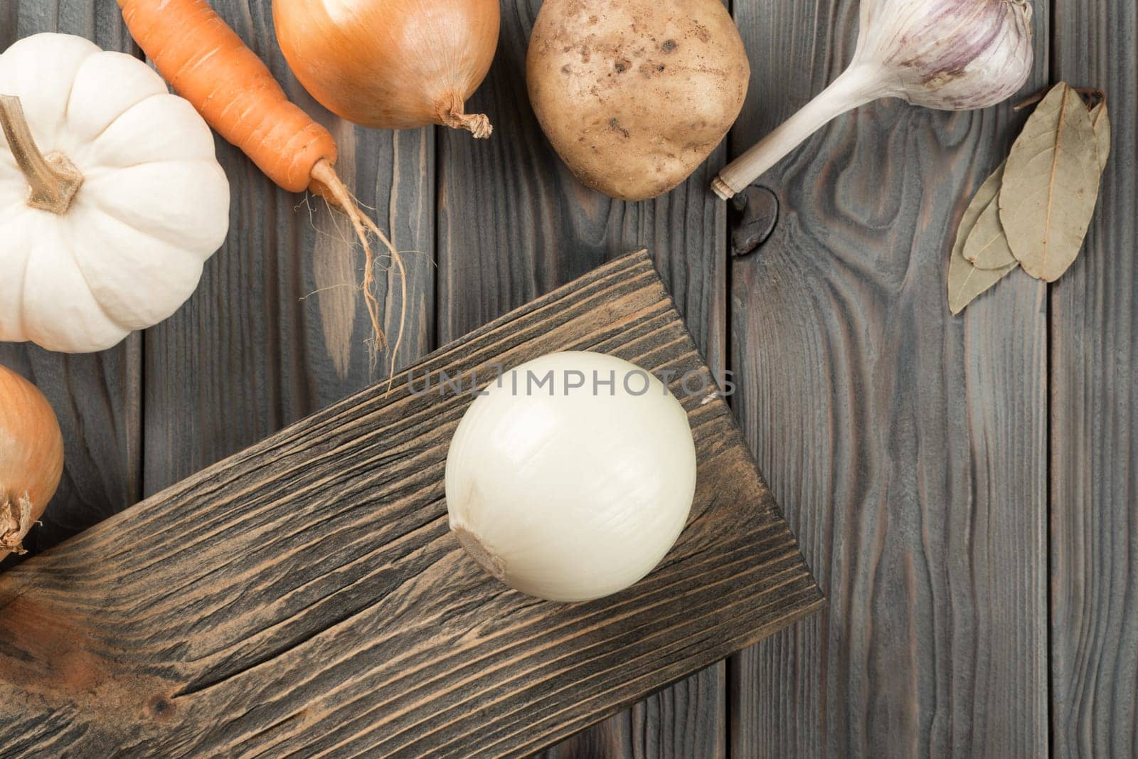 Spicy onion on kitchen wooden board. Whole white onion. Flat lay view. Layout of fresh raw vegetables and flavorings on table. Prepare ingredients for cooking. Healthy diet, foodstuffs.