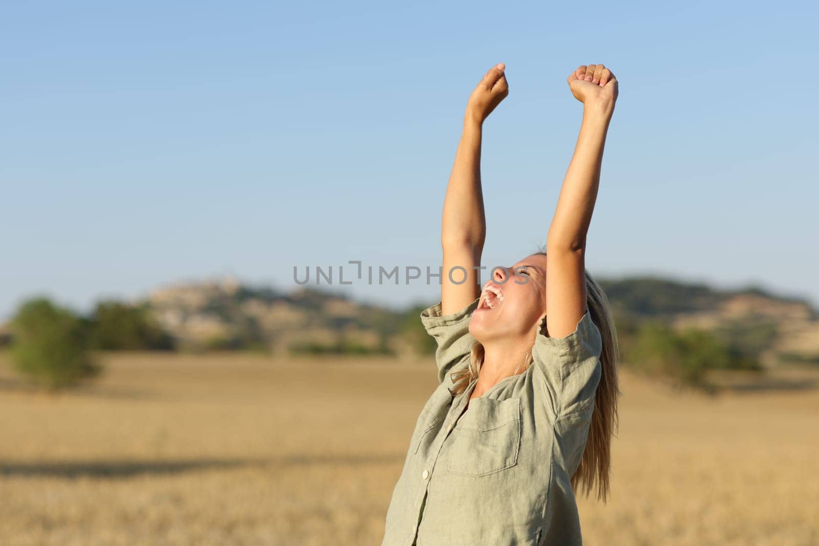 Teen raising arms in a golden wheat field at sunset