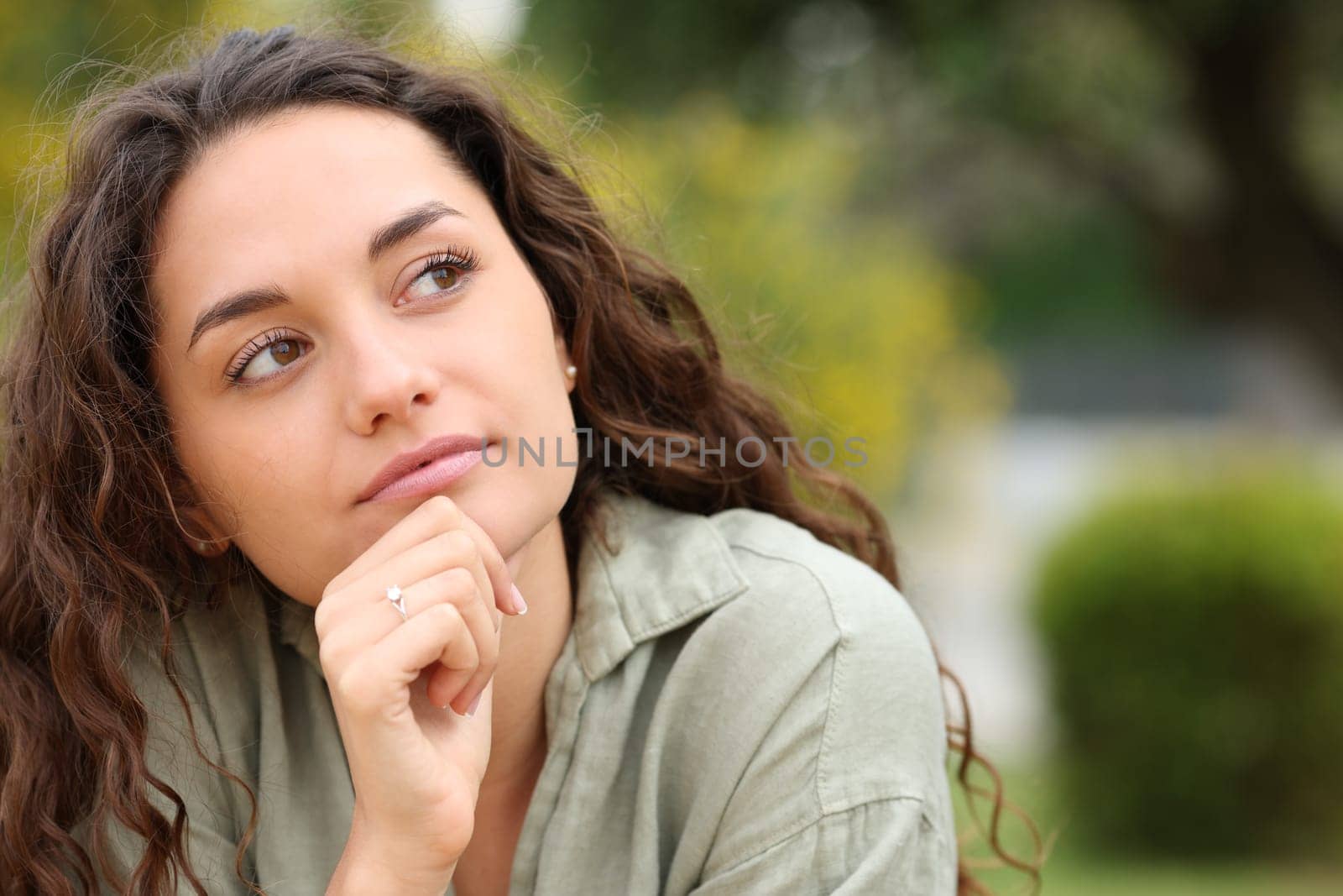 Front view portrait of a pensive woman looking at side in a park