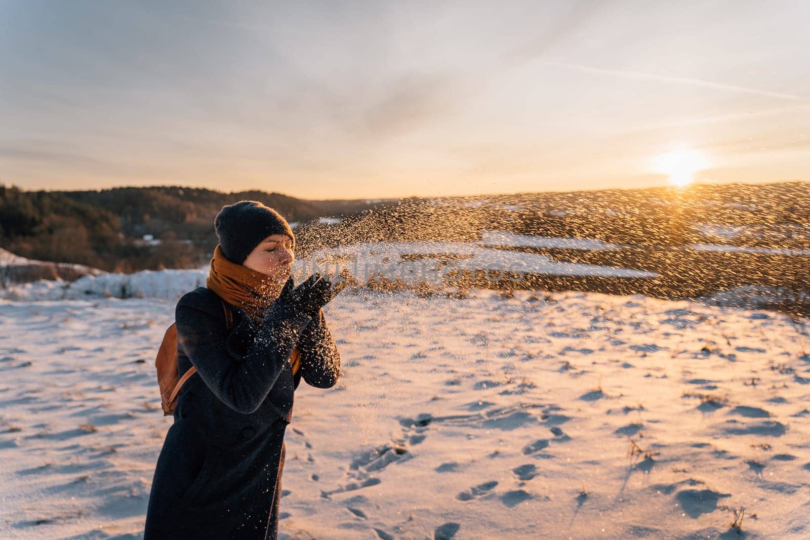 A woman blows snow from her palms on a sunny winter evening.