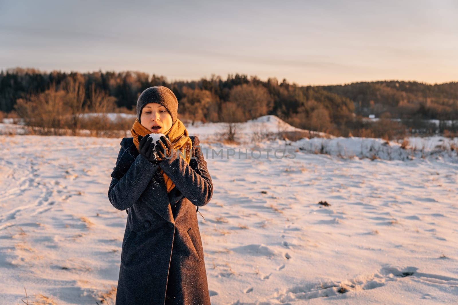 A woman in winter with a handful of snow in her palms prepared to blow it away.