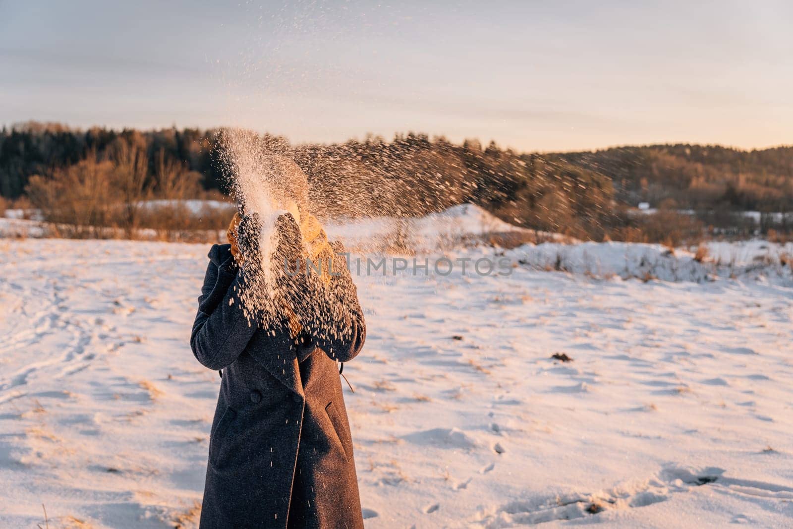 A woman with a closed face throws snow with her hands in a snow-covered field