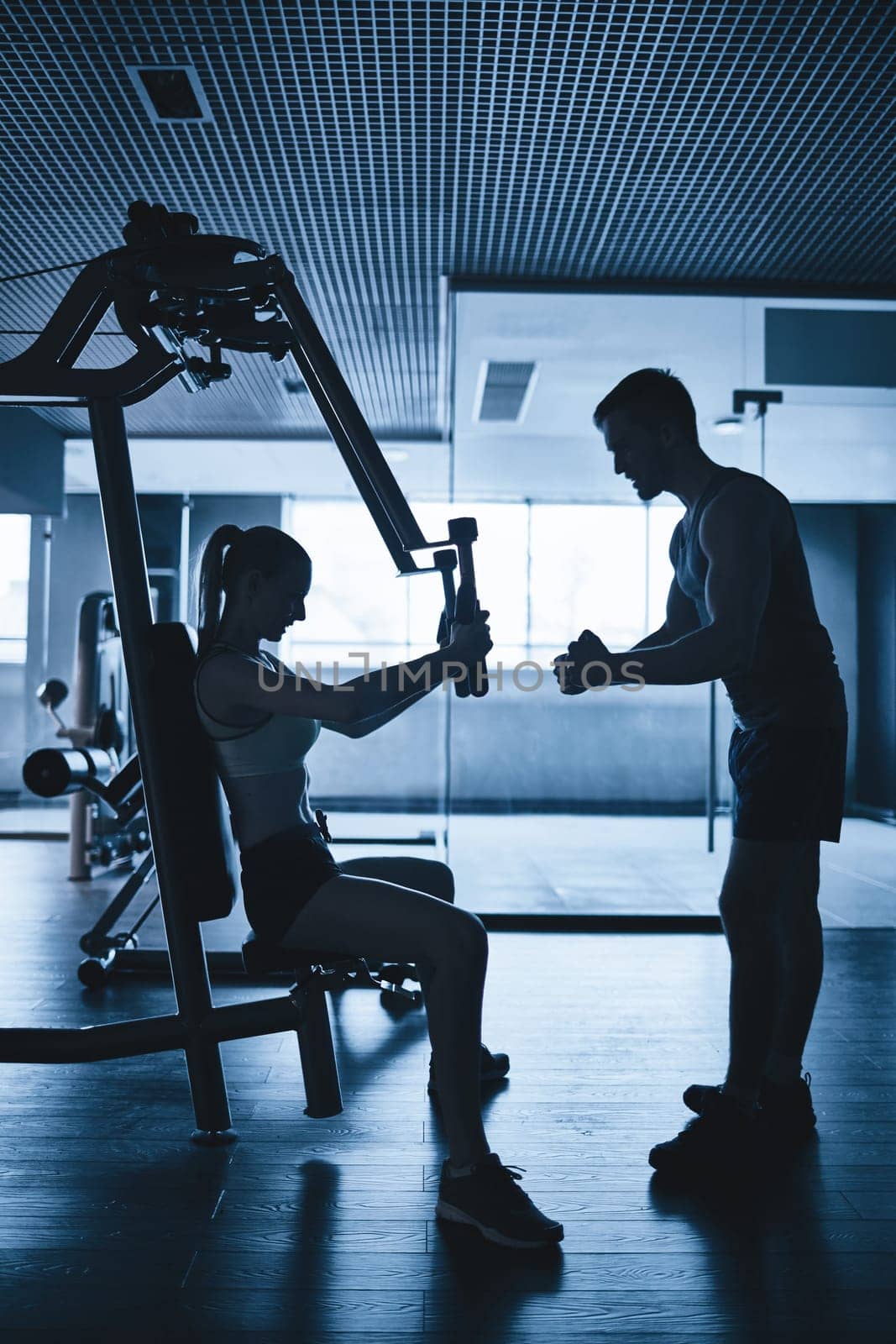 Fit female exercising in gym with help of her trainer