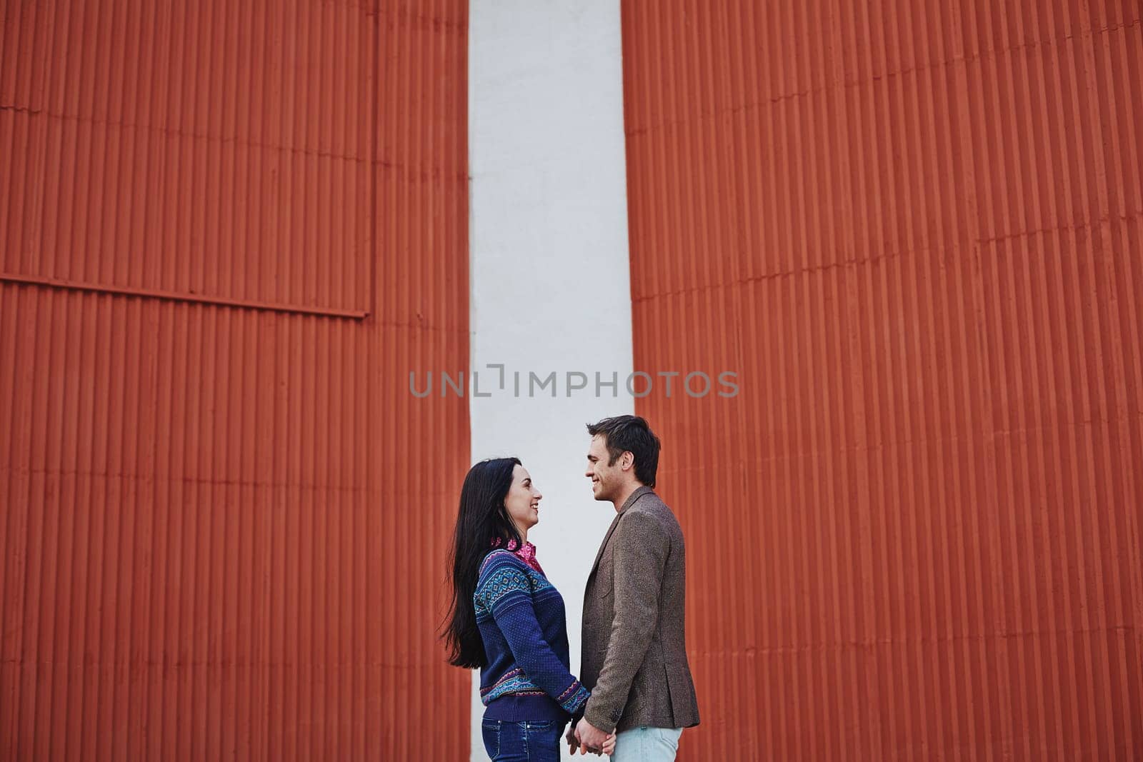 Young couple in casualwear looking at one another by wall