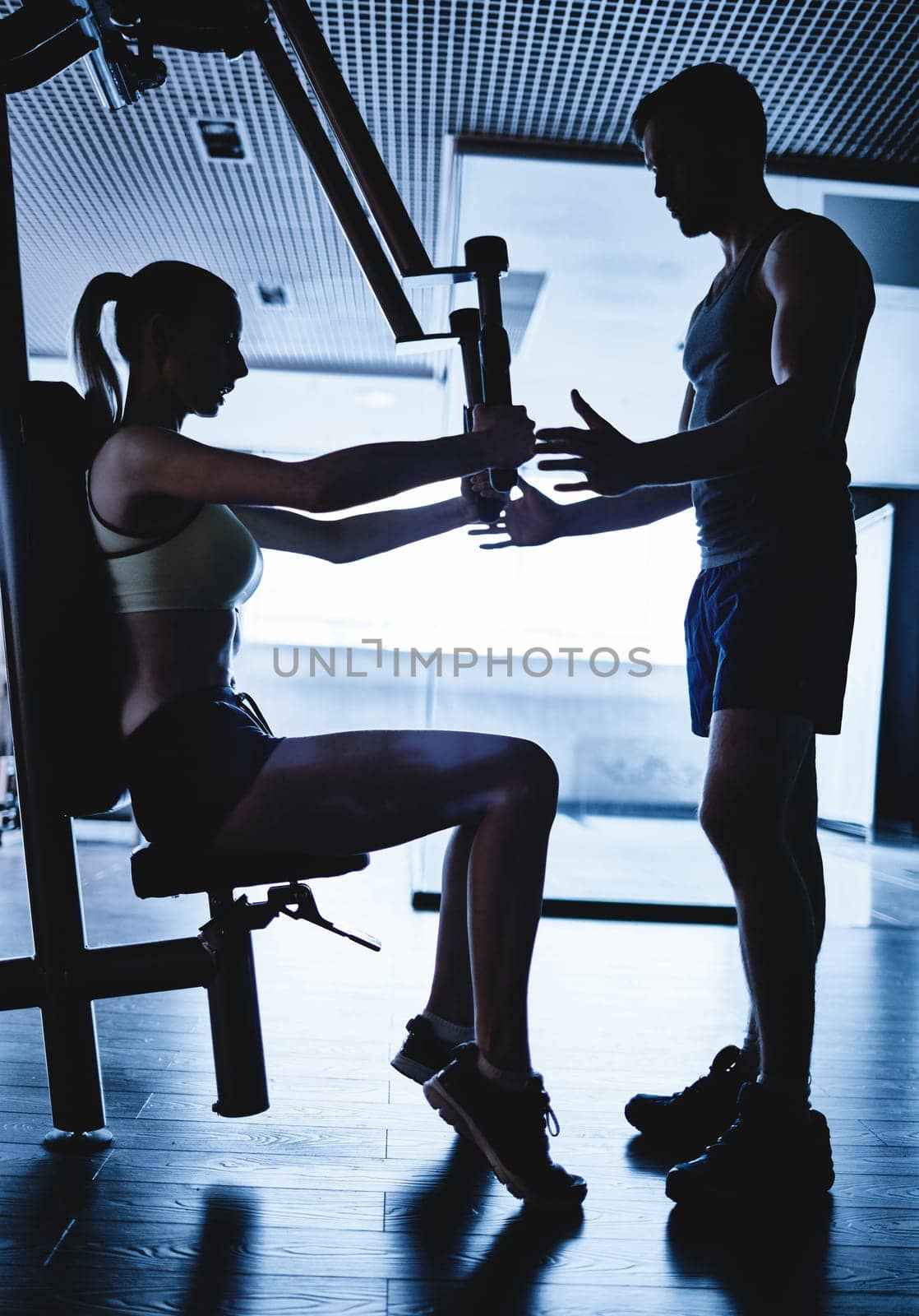 Trainer helping young woman to exercise on facilities