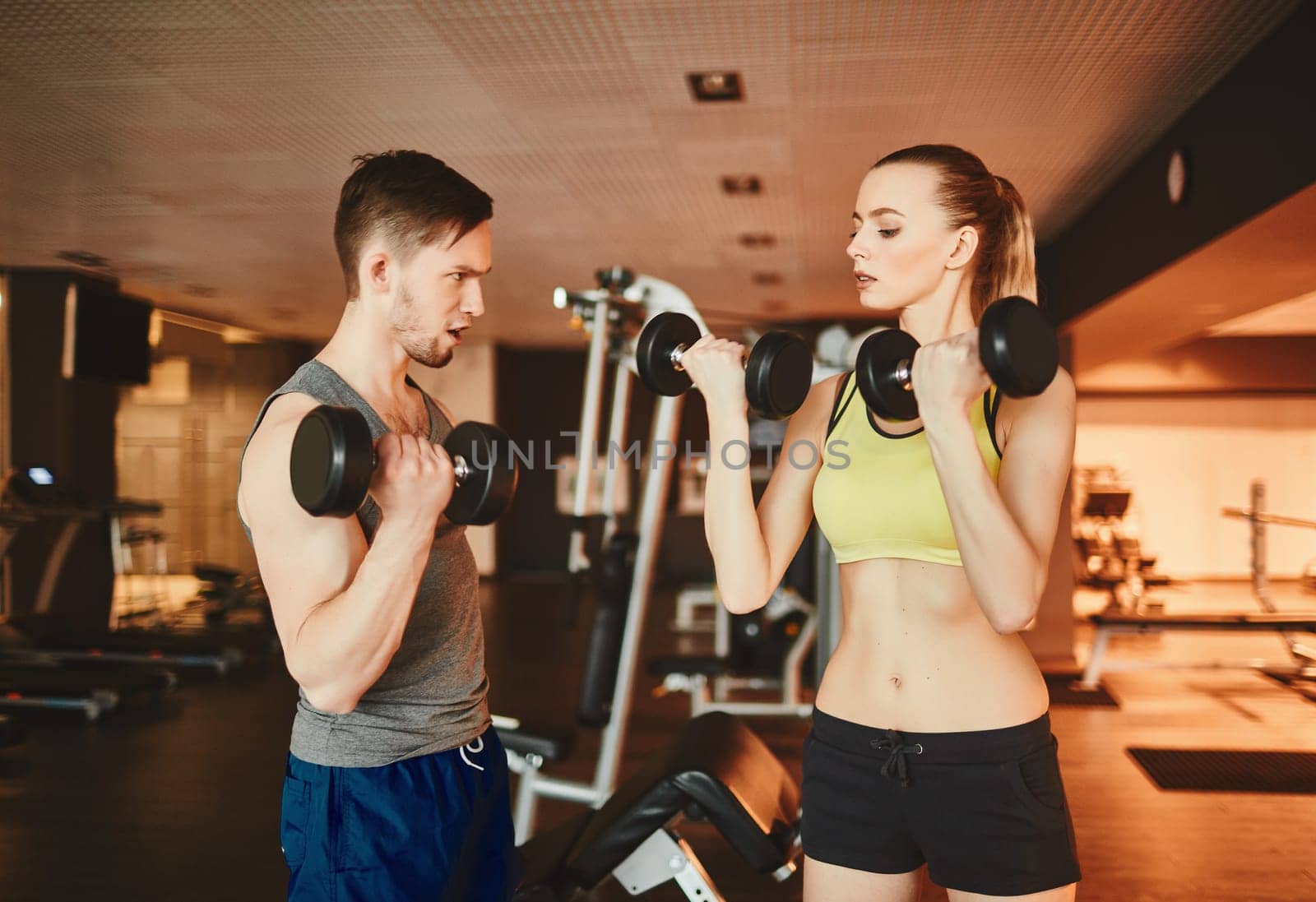 Fit woman exercising with barbells while young trainer consulting her