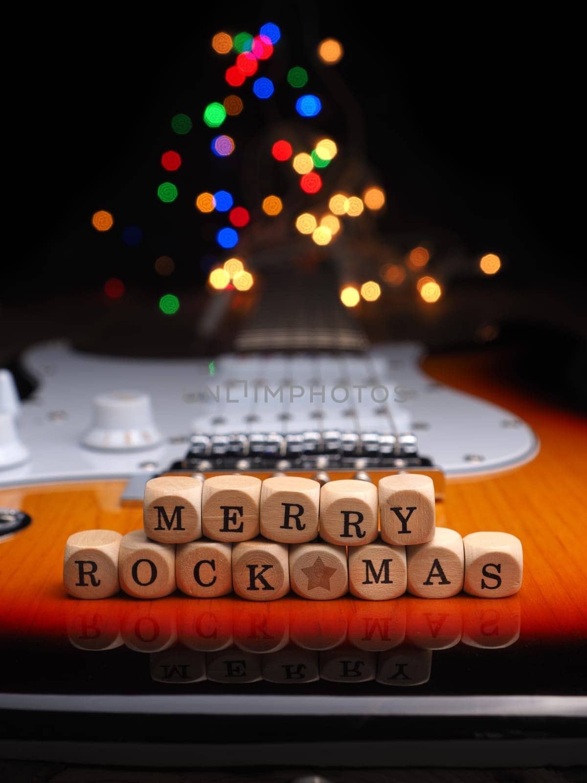 Wooden blocks with the inscription Merry Rock Mas on an old used vintage guitar with colorful Christmas lights bokeh background