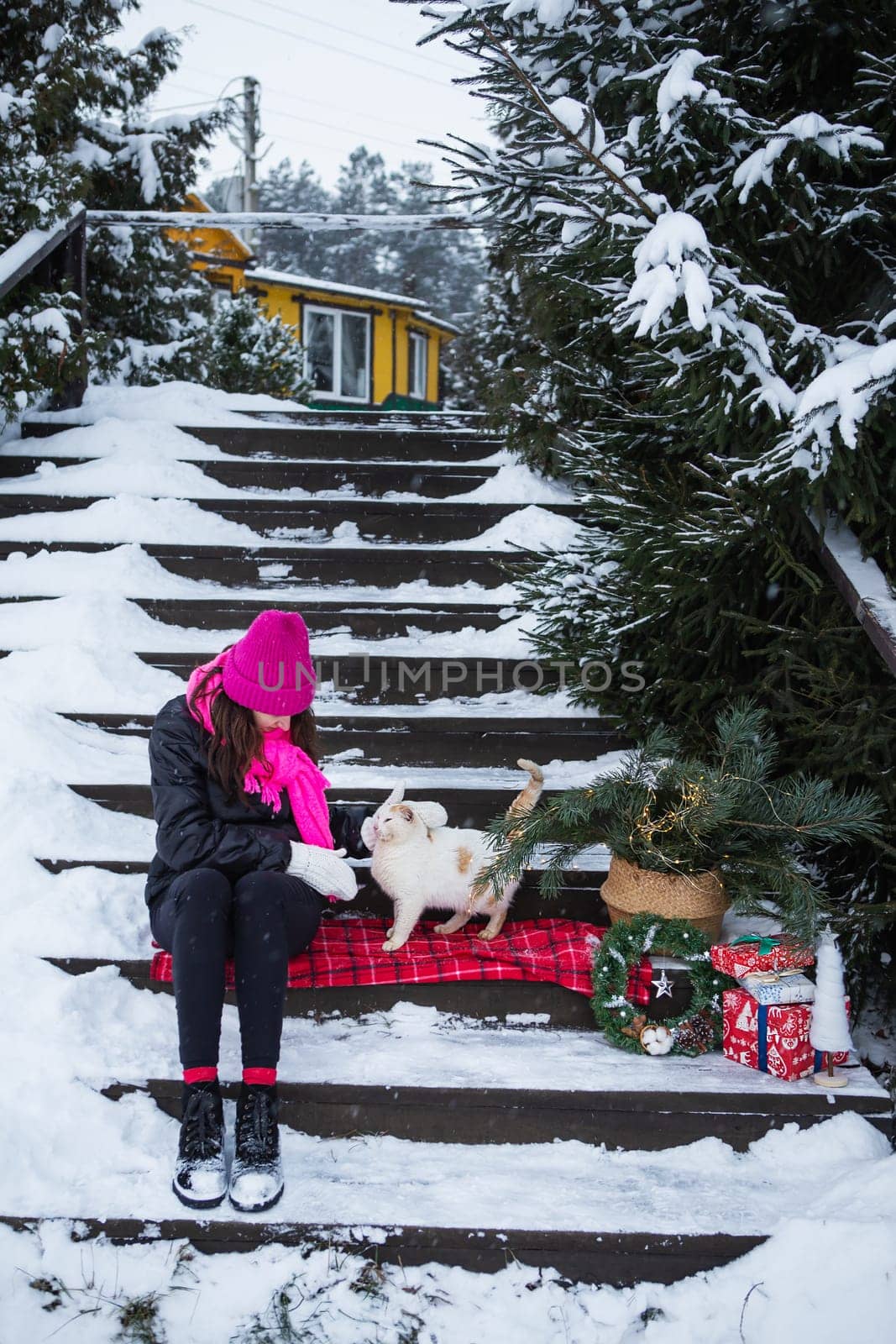 A woman holds and strokes a white and red fluffy cat near a Christmas tree in a basket, lights, gifts. New Year's magical atmosphere of coziness, love and warmth