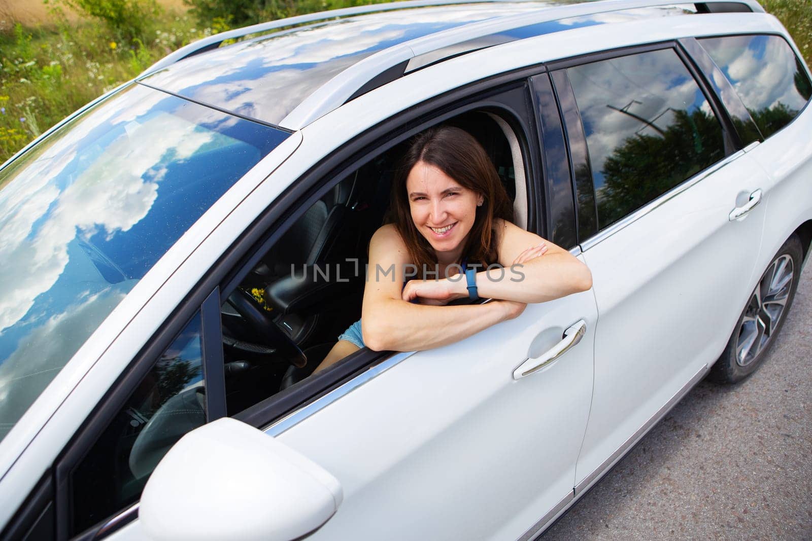 Young girl driving a car, the girl looks in the side mirror and smiles. Delivery for the right to drive a car