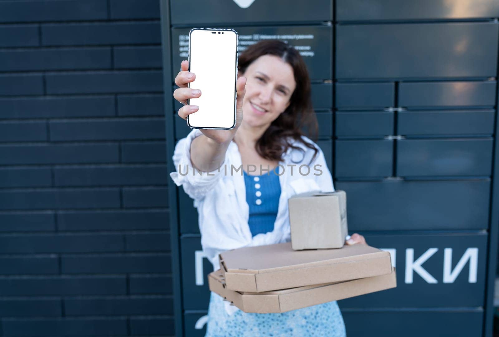 Happy woman holding mobile phone with white screen mockup for inscription and holding many different cardboard boxes with online order, satisfied with fast delivery, buying high quality products