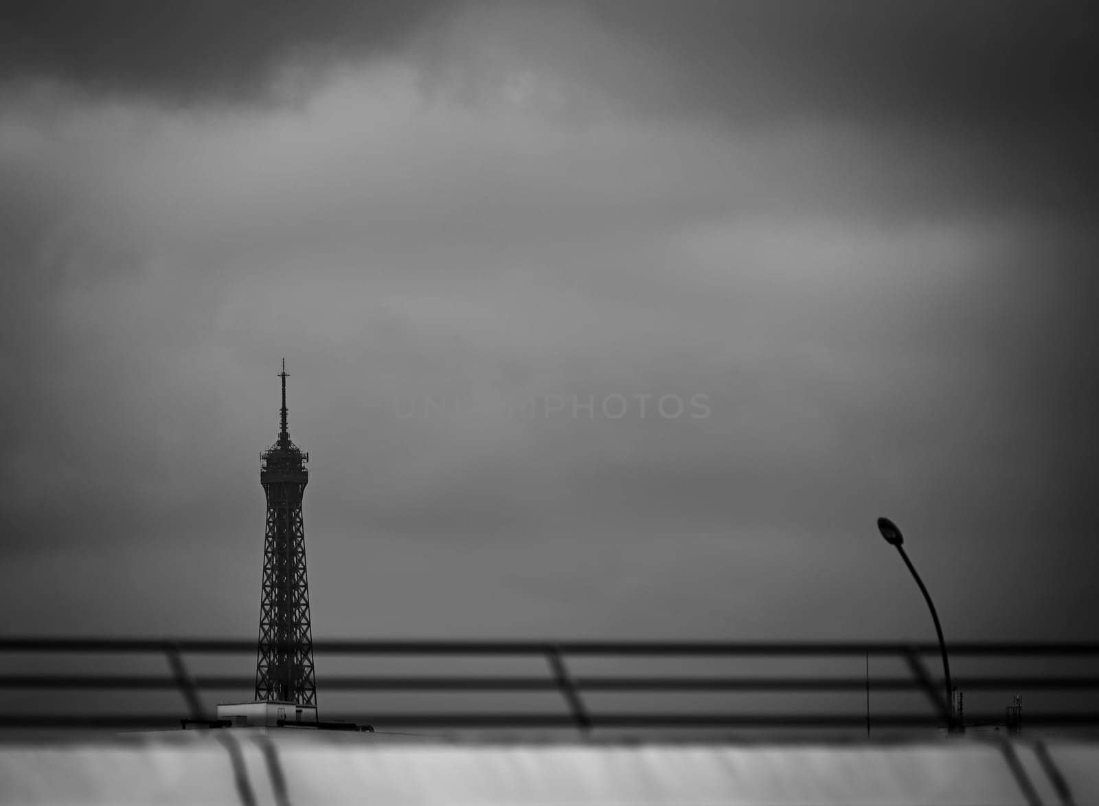 The iconic Eiffel Tower dominates the Paris skyline, shrouded in dramatic clouds, creating a striking contrast against the darkening skies. A streetlight partially frames this view.