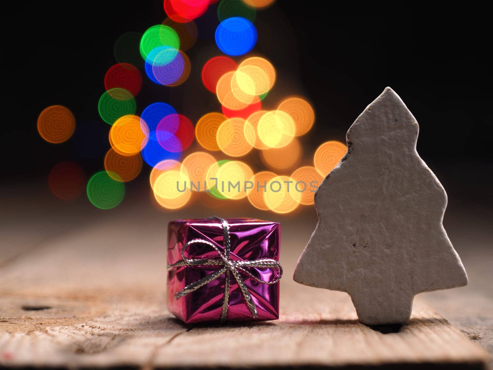 Close up of a pink gift box with a wooden tree shape on a colorful Christmas lights background
