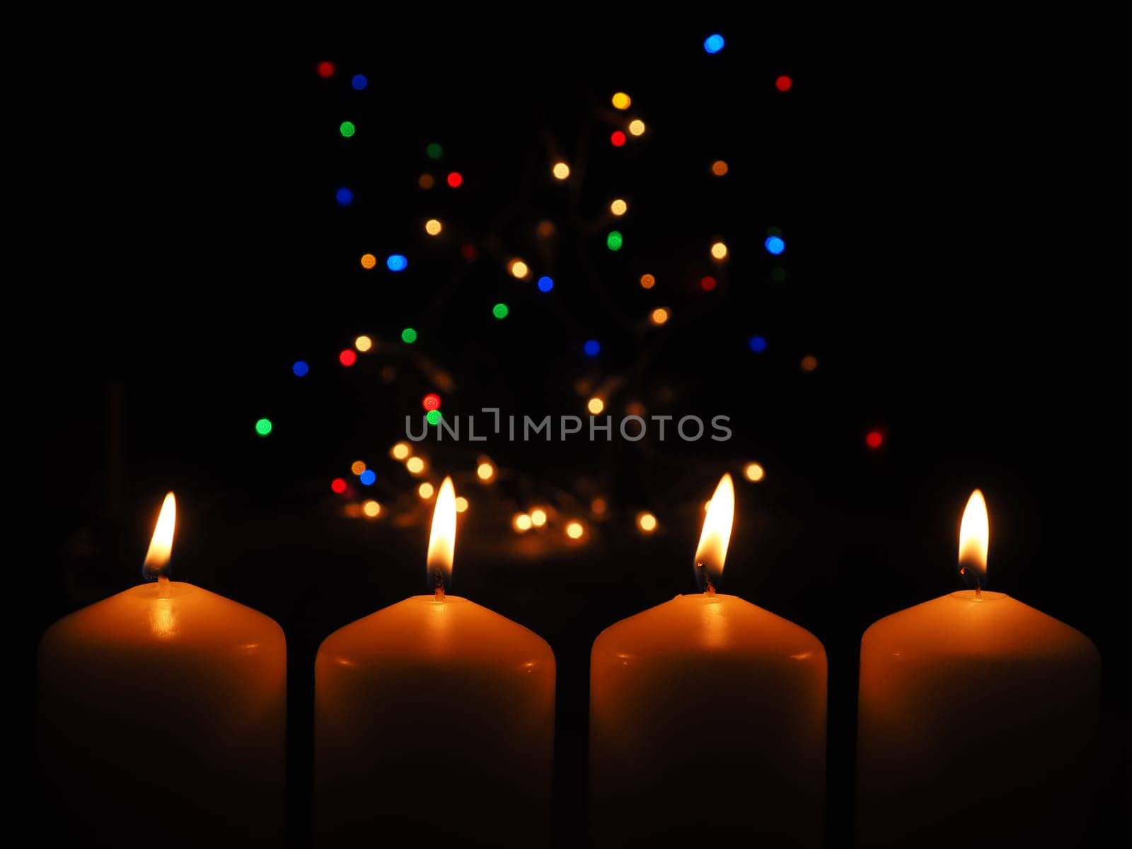 Four Advent candles burning with a colorful Christmas lights background, space for your text