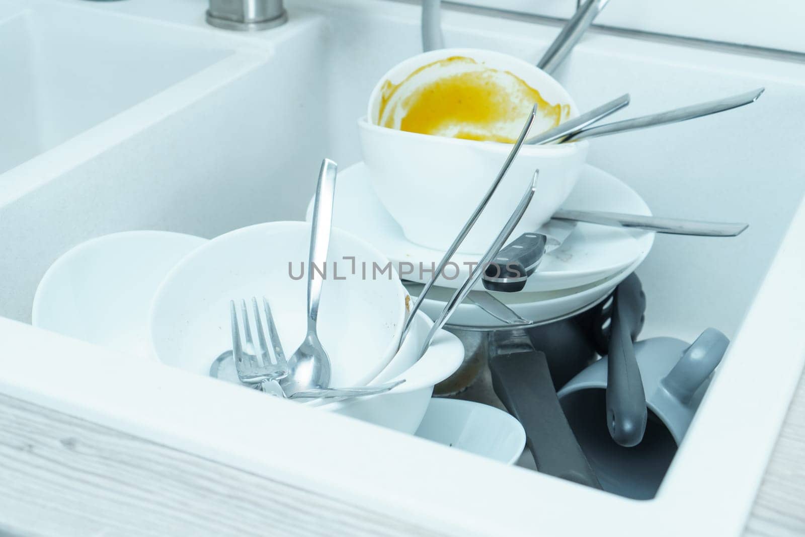 Close-up of white sink full of dirty white tableware, ceramic plates, bowls, knives, forks, spoons and grey cups. Cooking, housekeeping, cleaning, utensils, household chores, housework, washing dishes