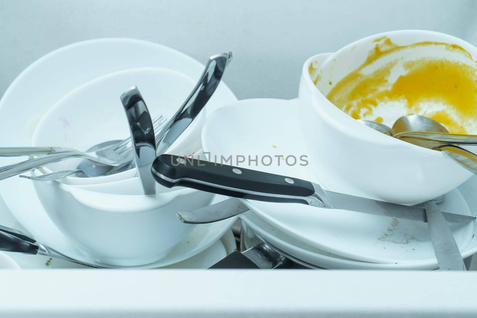 Close-up of white sink full of dirty white tableware, plates, bowls, knives, forks and spoon. Cooking, housekeeping, cleaning, utensils, household chores, crockery, cutlery, housework washing dishes