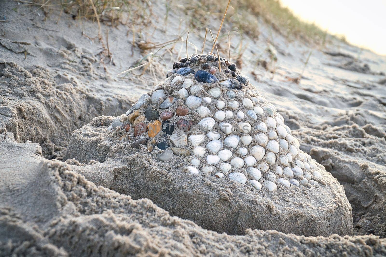 Sand castle with shells and sand. Moat around the castle in front of dunes. On the beach in Denmark by the sea. Landscape photo