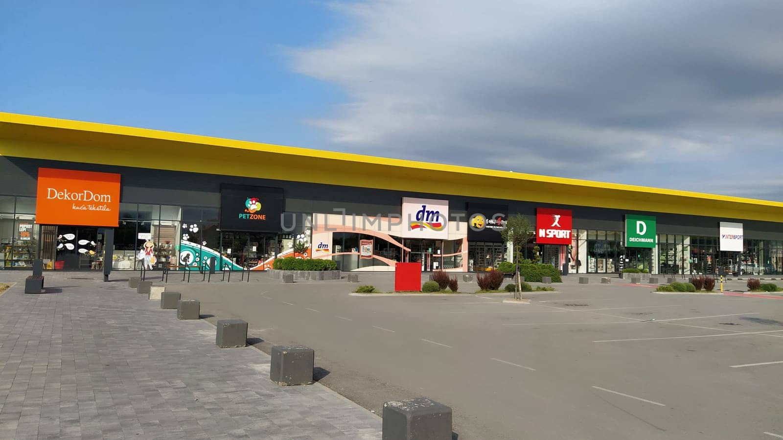 Stop shop shopping center, Sremska Mitrovica, Serbia, June 06, 2022. Square with open shops dm, intersport, dekordom, ccc, lc waikiki. People, parking and pavement. Sunny summer day.