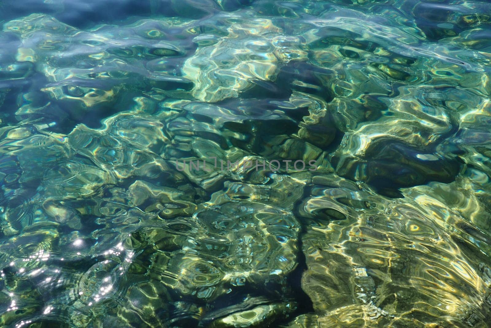 Green azure turquoise blue transparent sea salt water texture. Top view of the water surface and ripples. Water sea waves background. The rocky bottom with algae is visible through the crystal water.