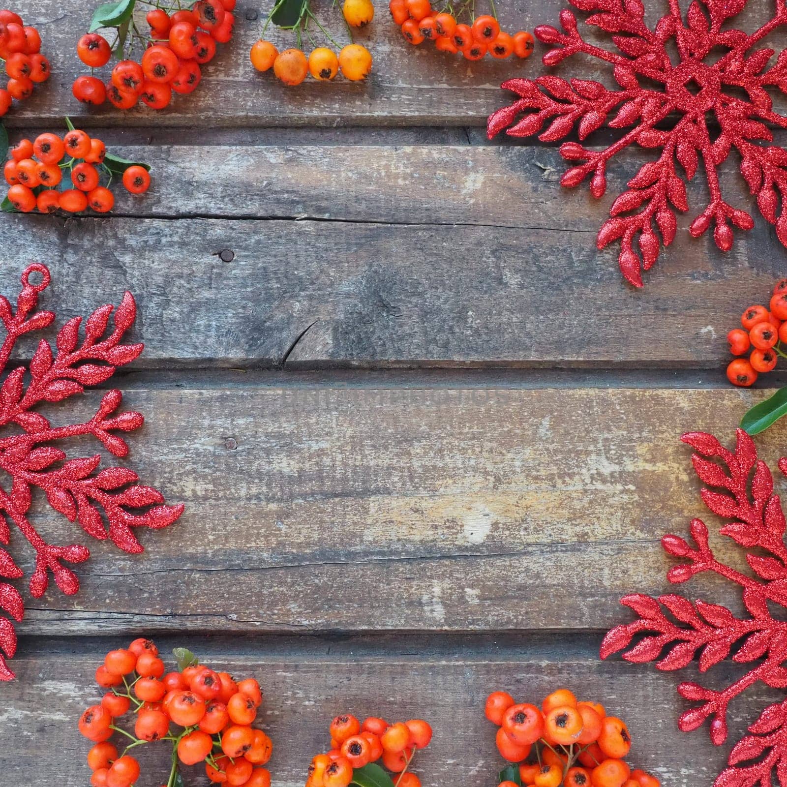 Red, orange and yellow winter rowan berries on a horizontal wooden background. Red shiny large snowflakes are arranged in circle around the edges background. New Year or Christmas natural backdrop.
