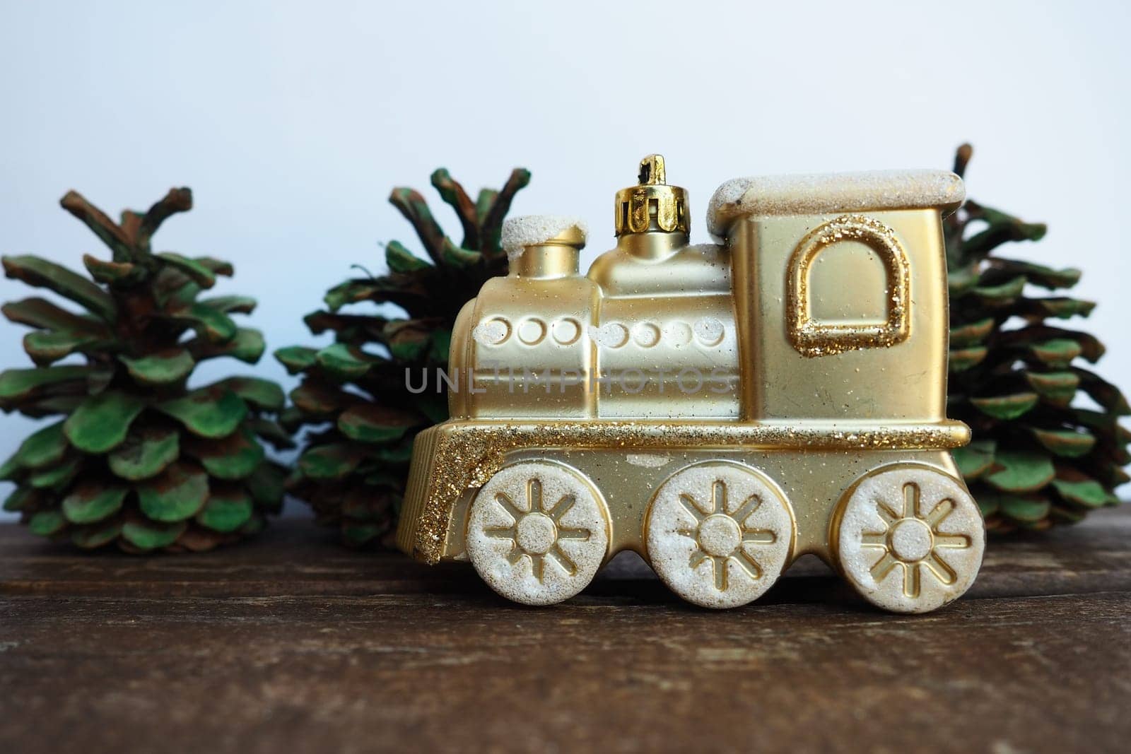 Golden children's toy train. Cones painted with green gouache like small Christmas trees. New Year or Christmas card. Icicles and snow on the train. Festive background. Christmas decorations.
