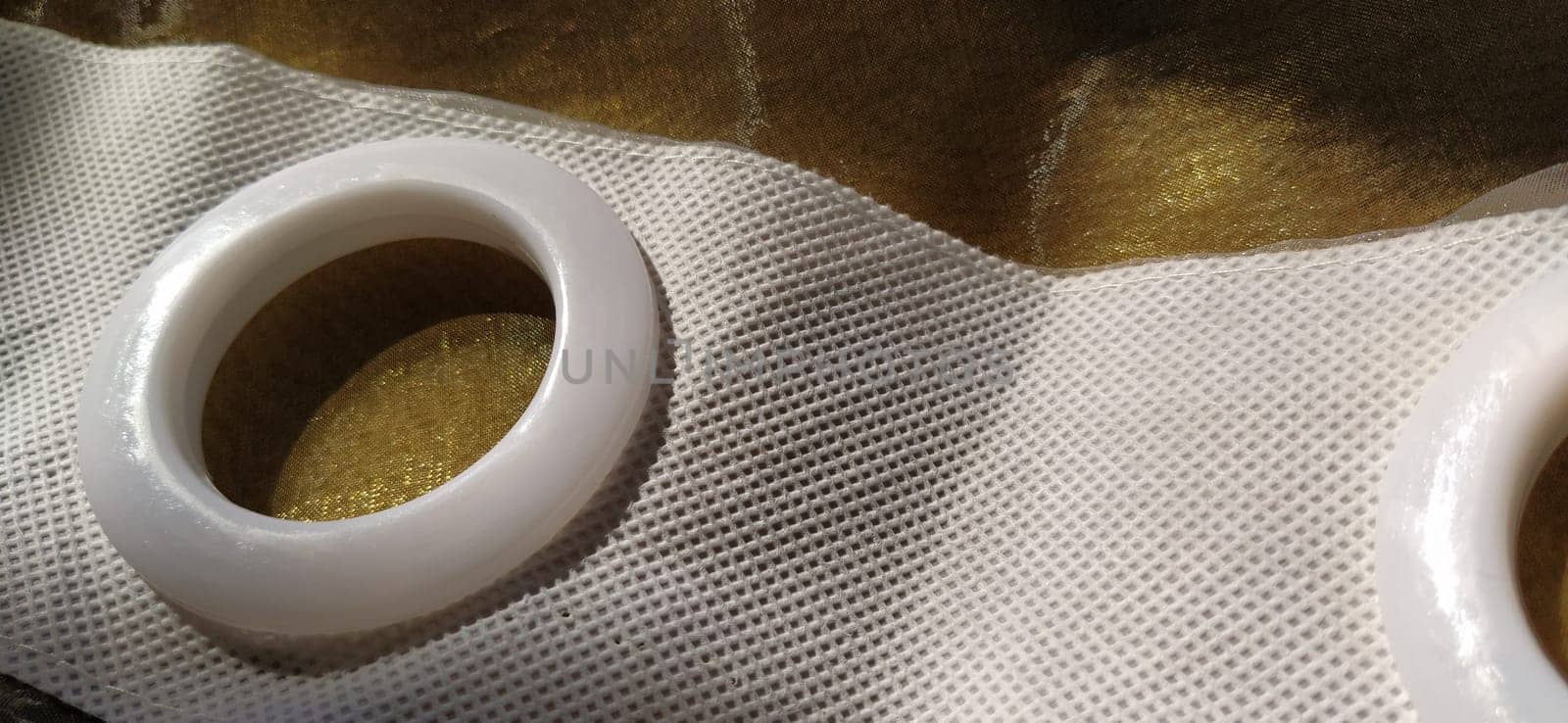Plastic rings for attaching the fabric to the curtain rod. White plastic organza tulle eyelets. Light curtain in beige, brown or orange colors. White non-woven fabric. Finished textile edge. Interior element
