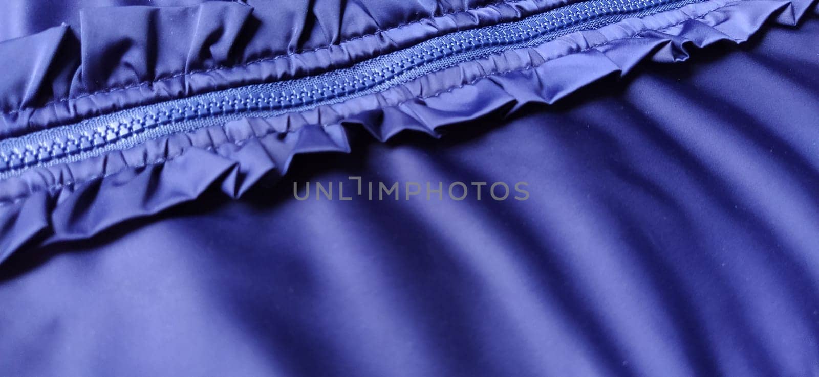Buttoned zip on a blue raincoat. Waves and folds in the fabric. Beautiful flounces, ruffles, frills. Decorative finishing of a garment. Smocked, sewn silk fabric. Nice casual wear