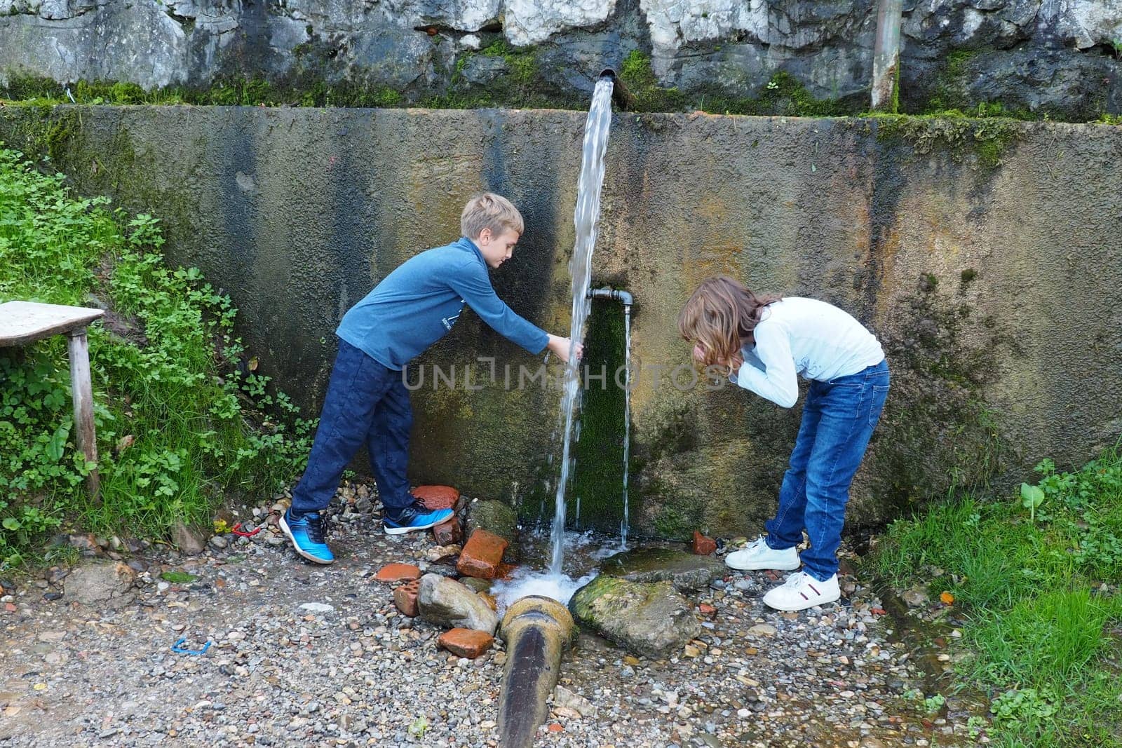 Banja Koviljaca, Loznica, Serbia Mount Guchevo park and forest. Source of mineral sulfuric and ferruginous water Ilidja Chesma Cesma. A jet of water pours out of a tap in a concrete wall. Boy and girl