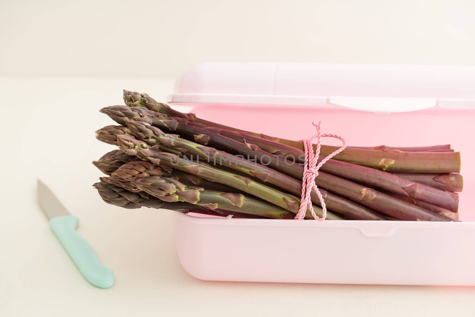 Bunch of purple asparagus in plastic tin with kitchen knife