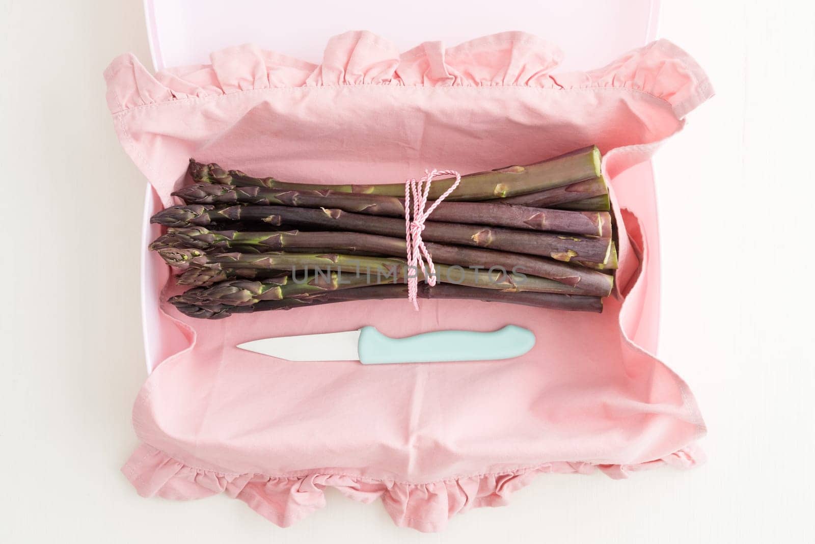 Bunch of purple asparagus in plastic tin with kitchen knife
