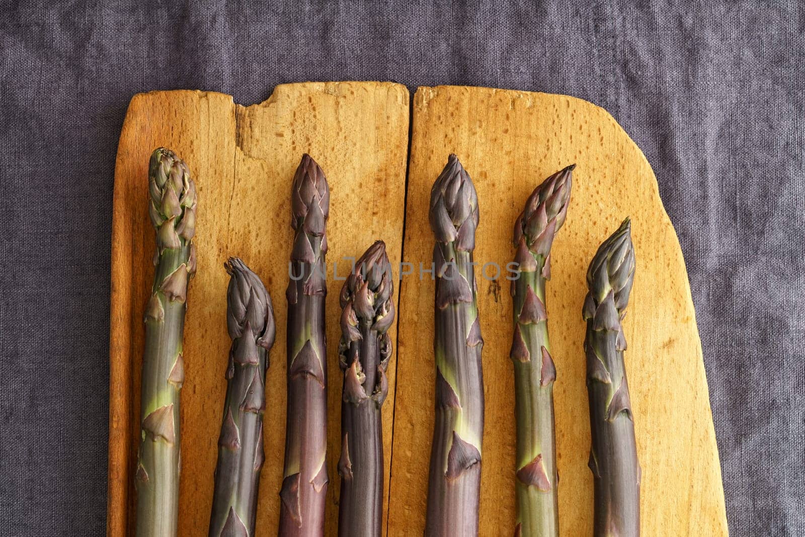 Fresh violet asparagus on an old wooden board on linen in a dark light mood