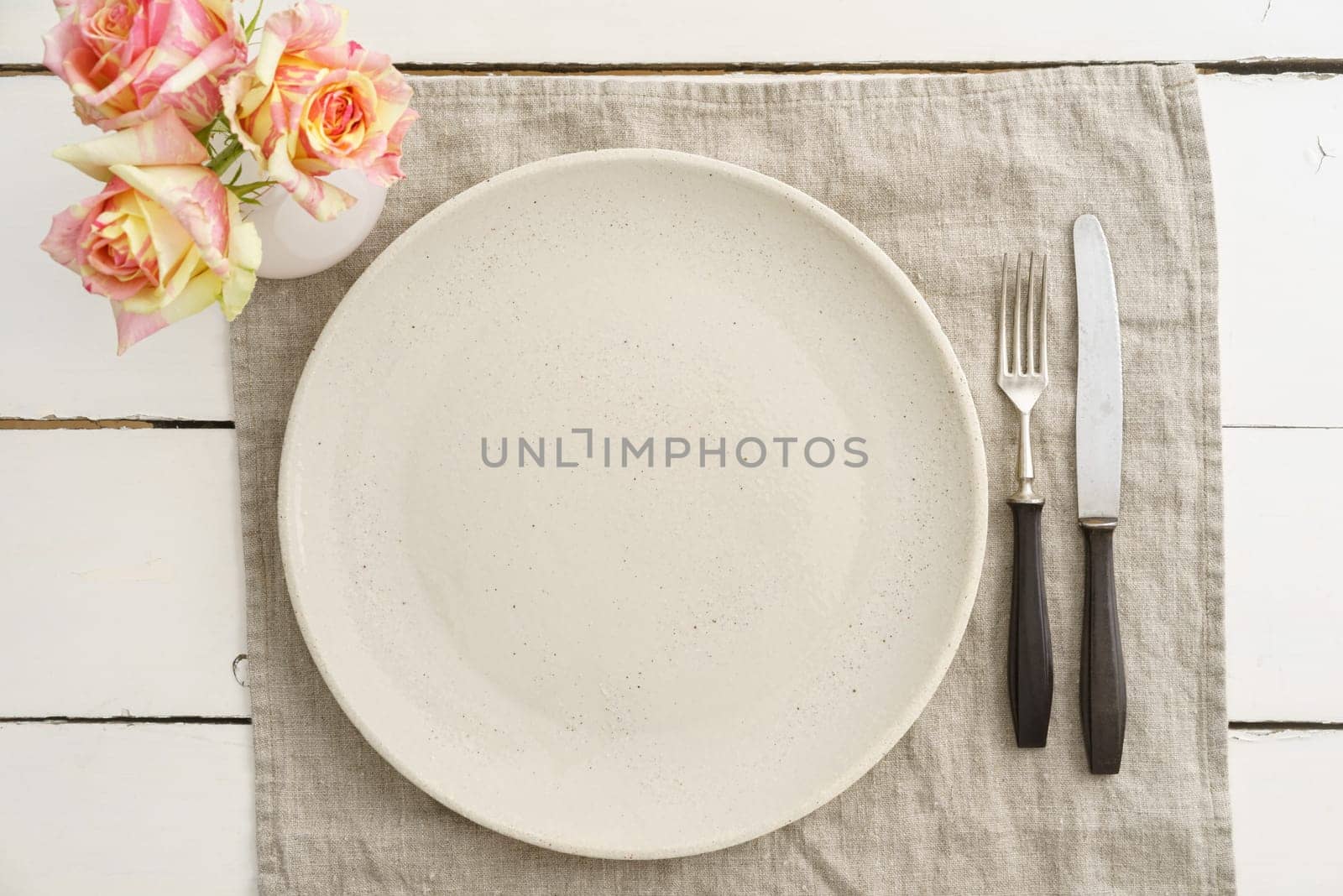 Empty cream plate with old cutlery on linen napkin with roses