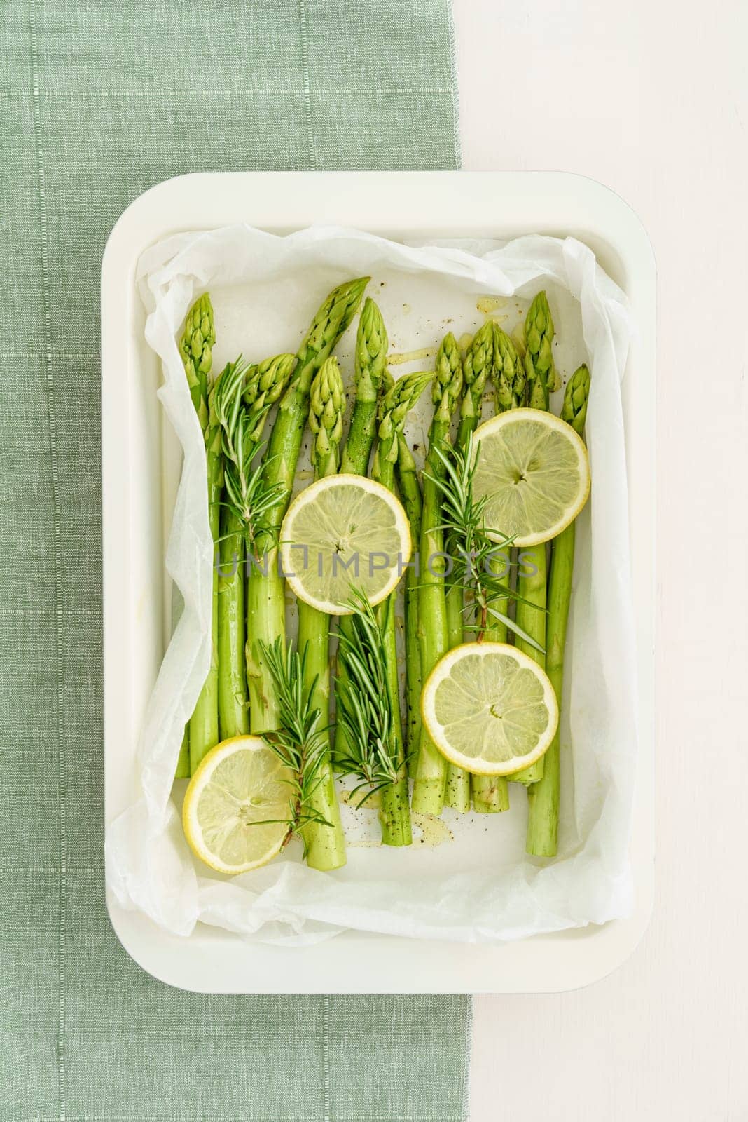 Green asparagus with lemon slices for baking with baking paper in a baking dish