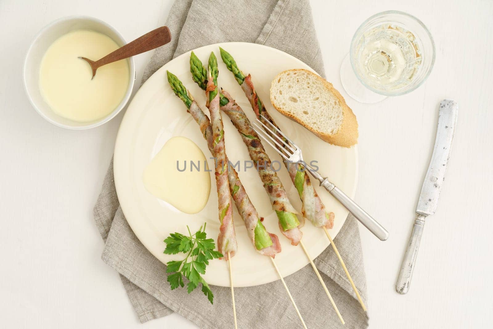 Bacon-wrapped grilled green asparagus skewers with Hollandaise sauce,baguette and white wine