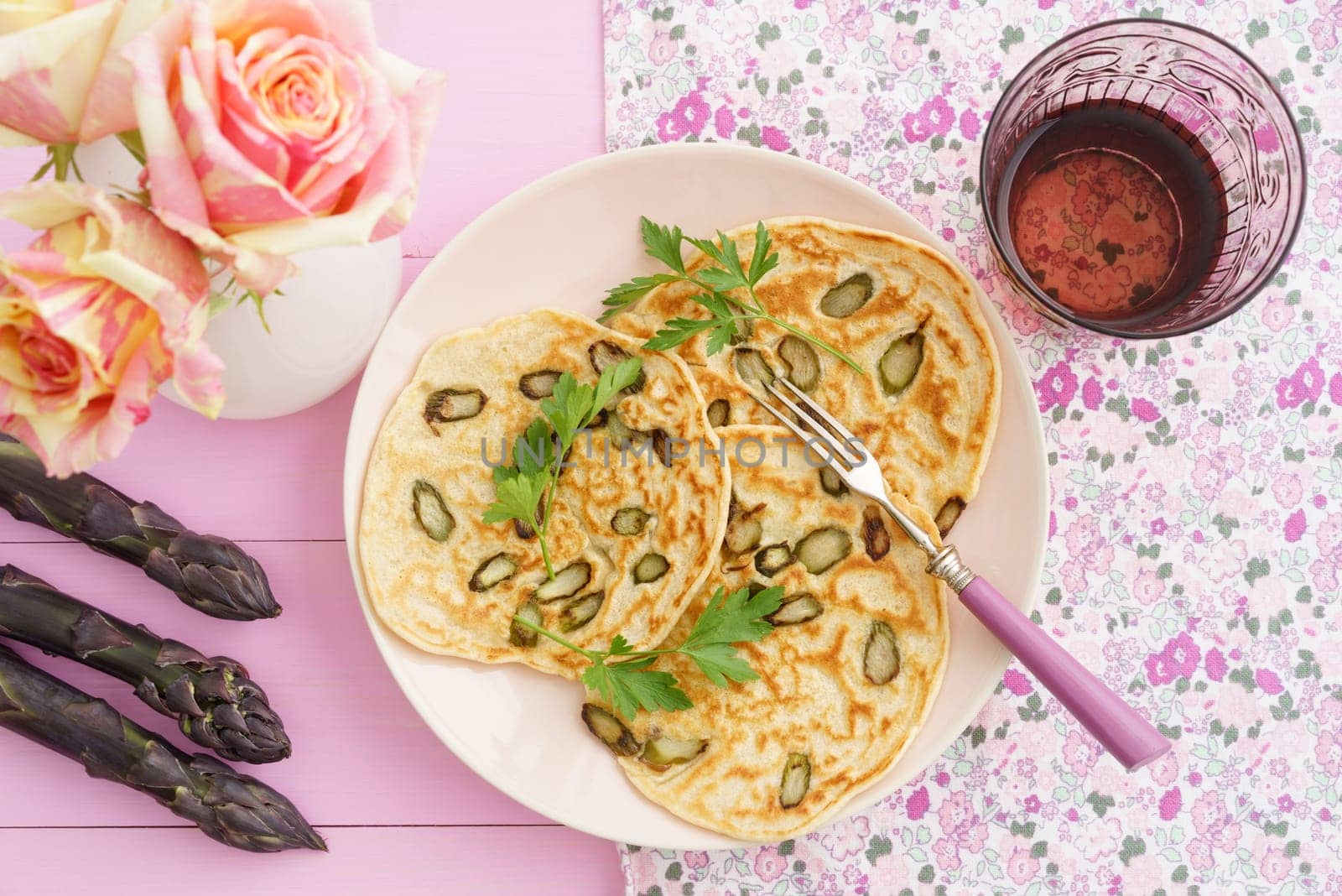 Pancakes with violet asparagus on pink plate with roses