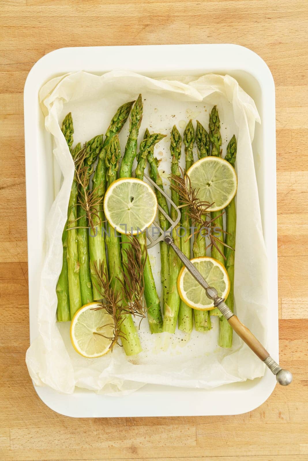 Baked green asparagus with slices of lemon with baking paper in a baking dish