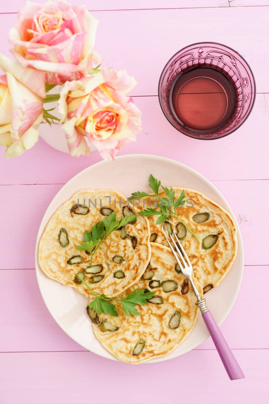 Pancakes with violet asparagus on pink plate with roses