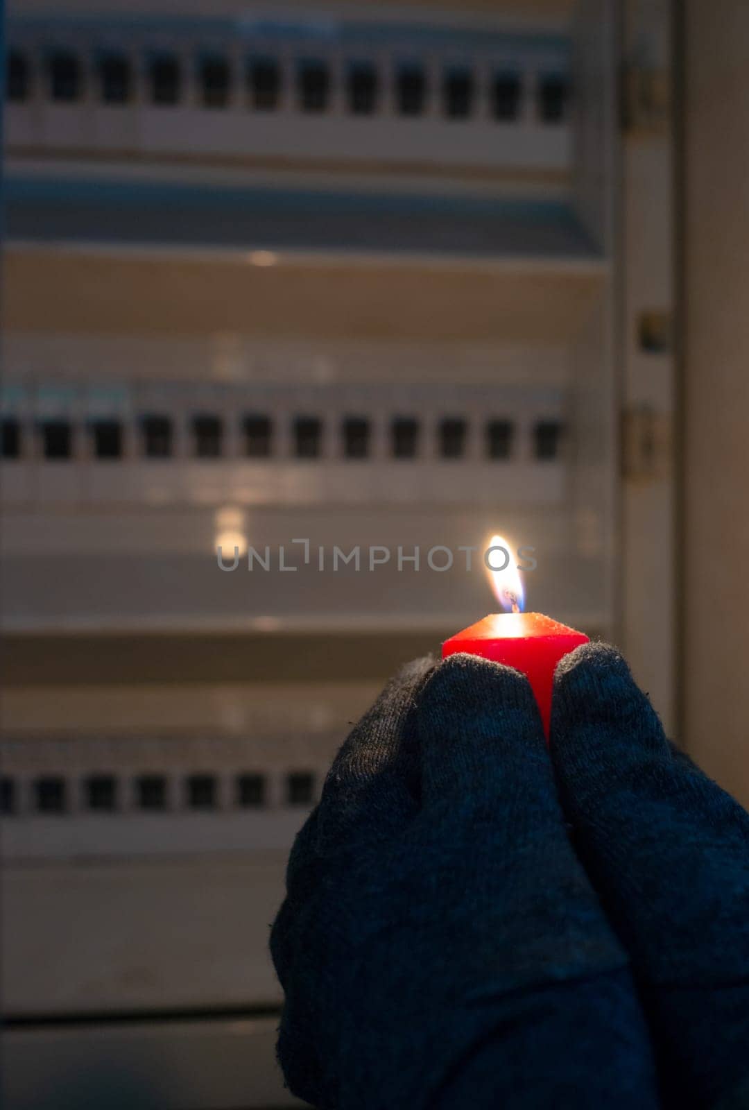Blackout, standing with a candle in front of a power fuse box, energy cut out, uncertain supply, risk and crisis for electricity