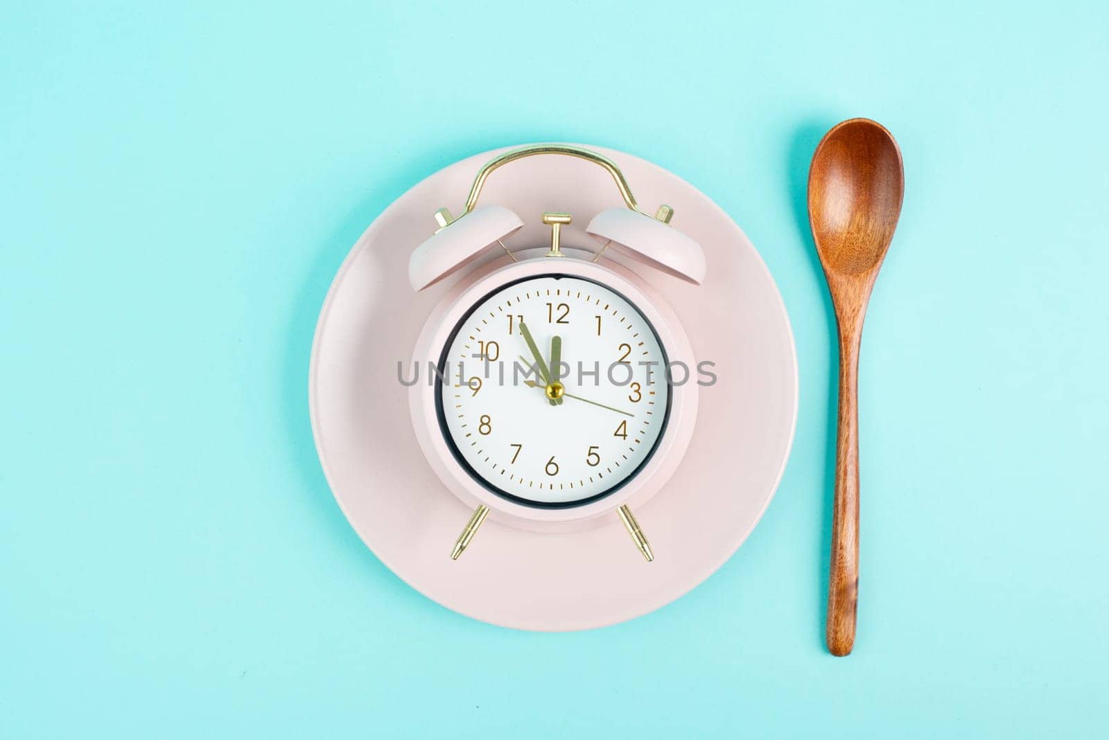 Alarm clock on a plate with a spoon in old retro style, pastel color, time to wake up in the morning, having lunch, taking a break